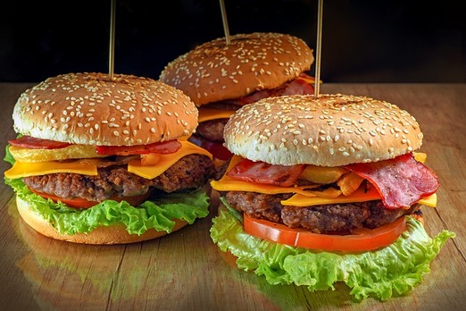 Drei saftige XXL Burger mit Rindfleisch, Käse, Salat, Tomaten und knusprigem Speck auf einem Holztisch – frisch zubereitet bei Deniz Pizzahaus in Bruck an der Leitha.
