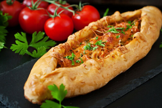 Traditionell gebackene Pide mit würzigem Fleisch, geschmolzenem Käse und frischen Kräutern auf schwarzer Servierplatte – Spezialität von Deniz Pizzahaus in Bruck an der Leitha.